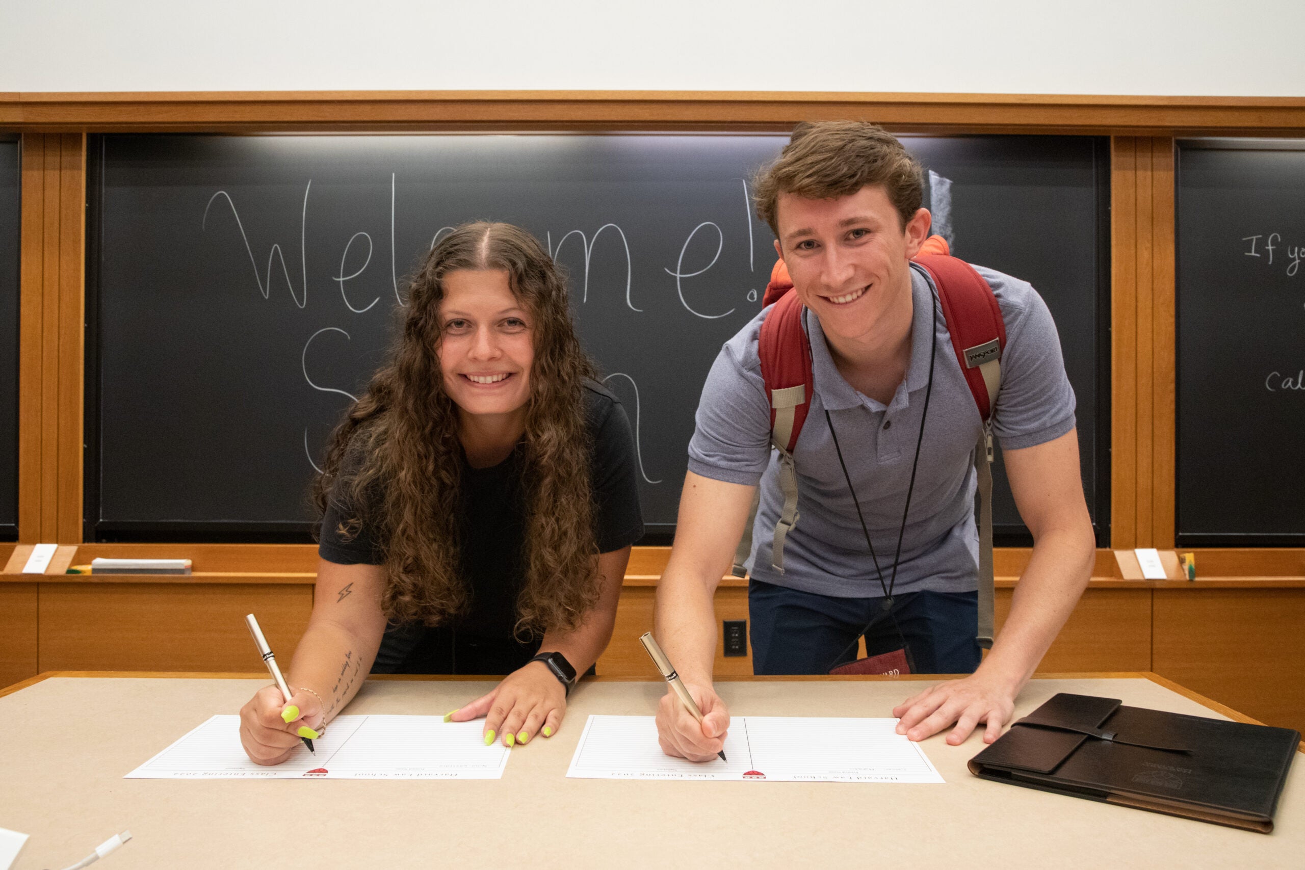 Two students smiling and signing a sheet of paper.