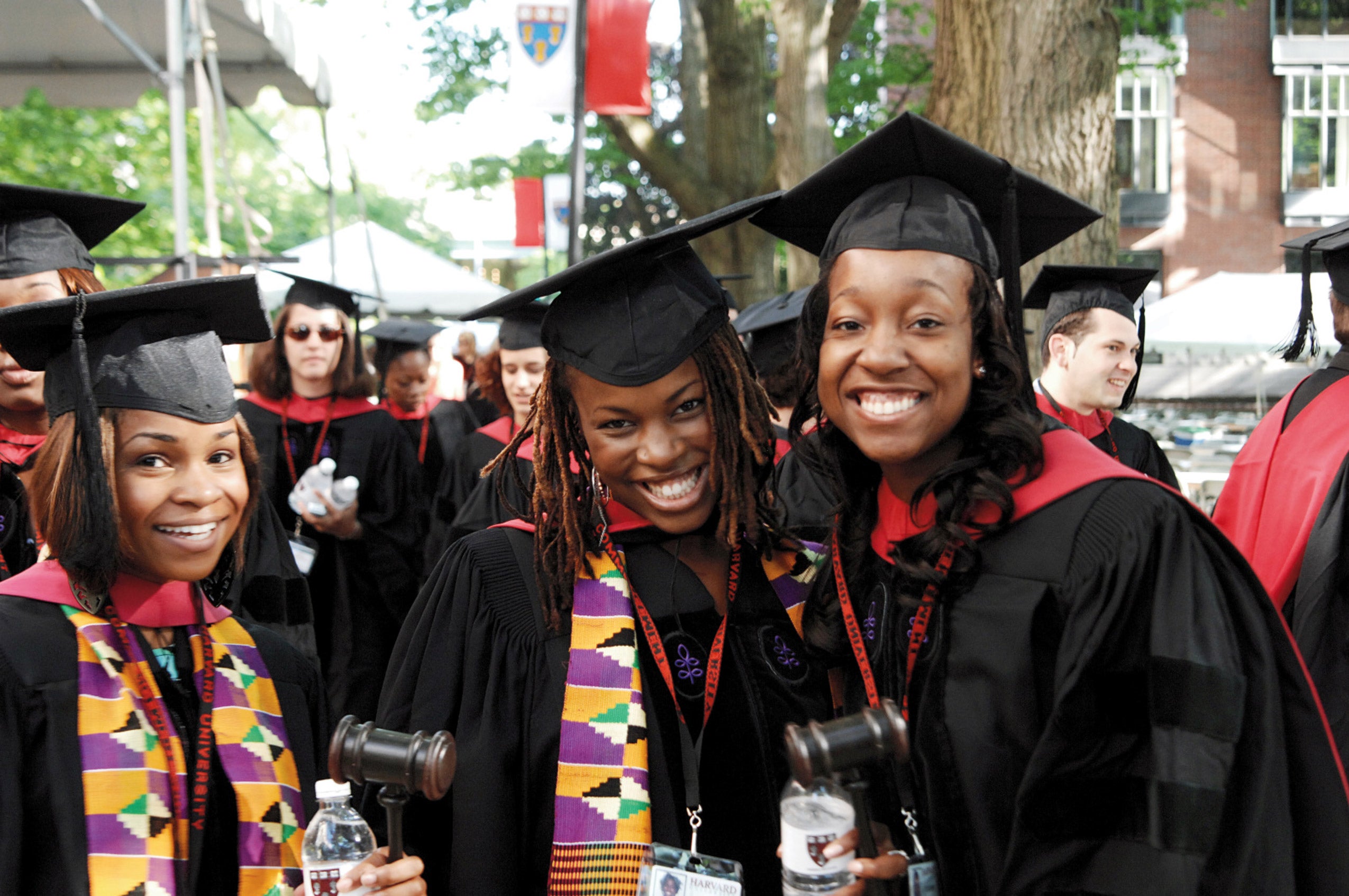 Three graduates in black robes pose for the camera on campus