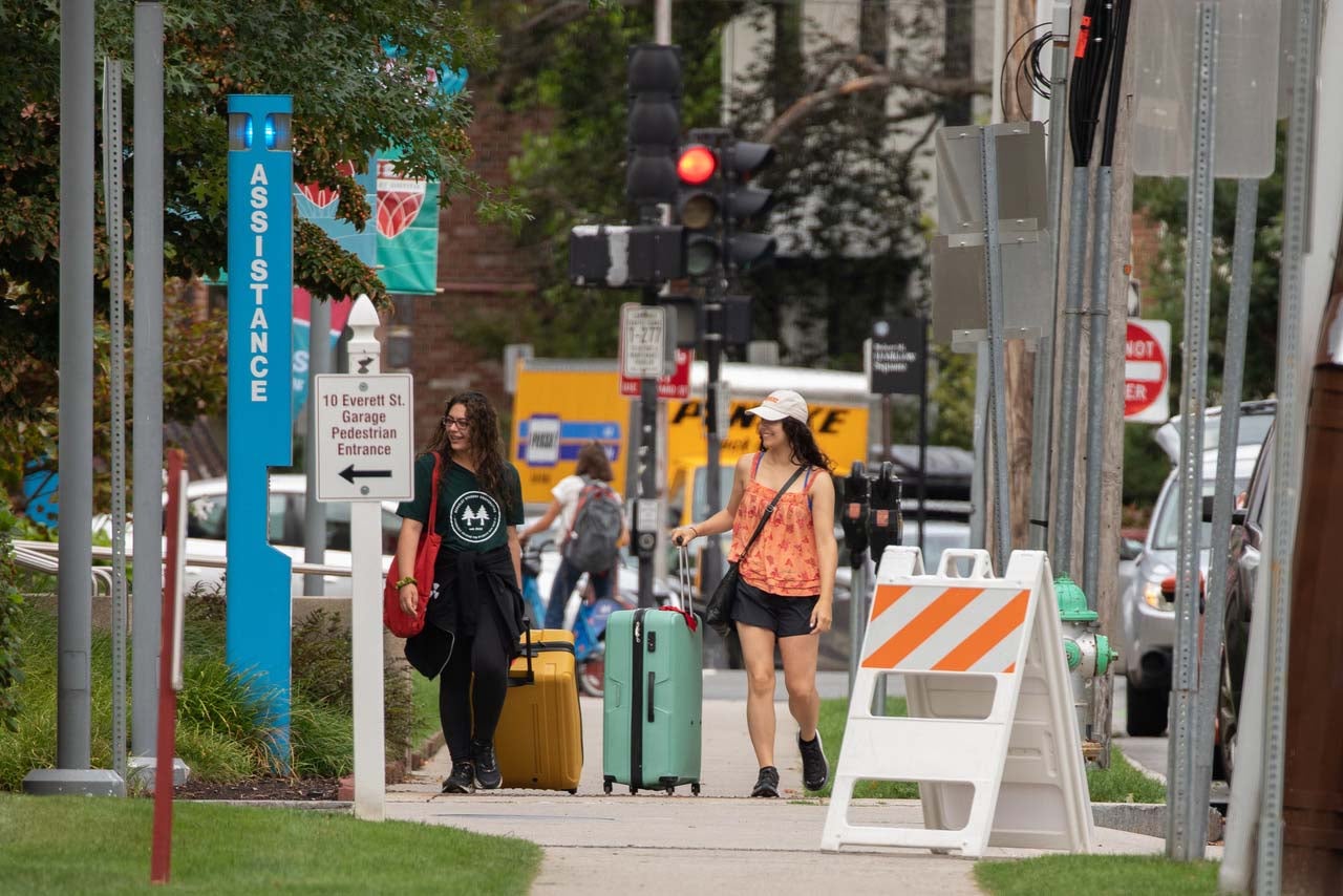 Two women roll their suitcases down a city street.