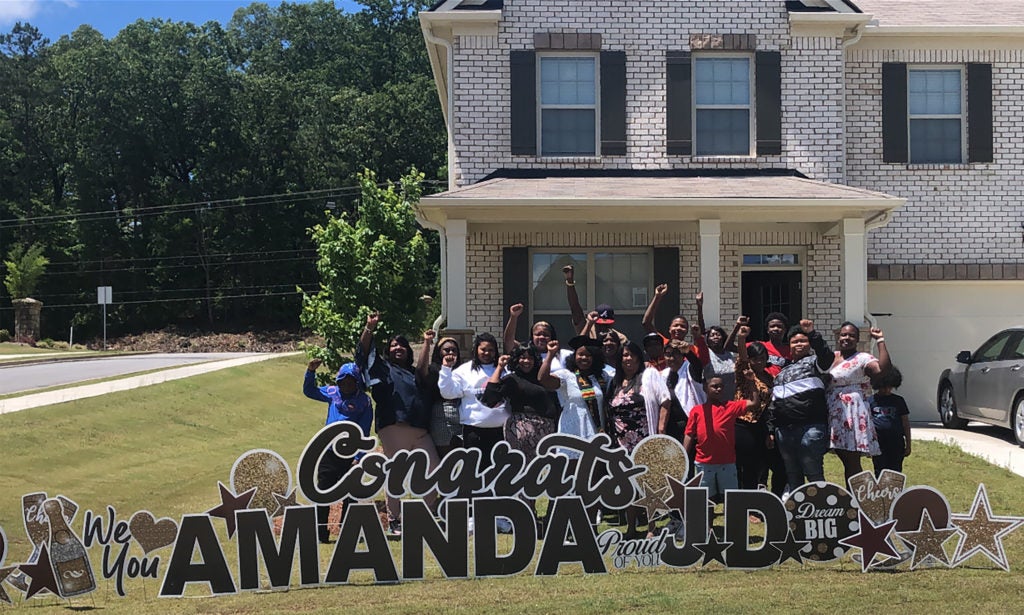 A large group of people pose behind a large sign that says Congrats Amanda J.D.
