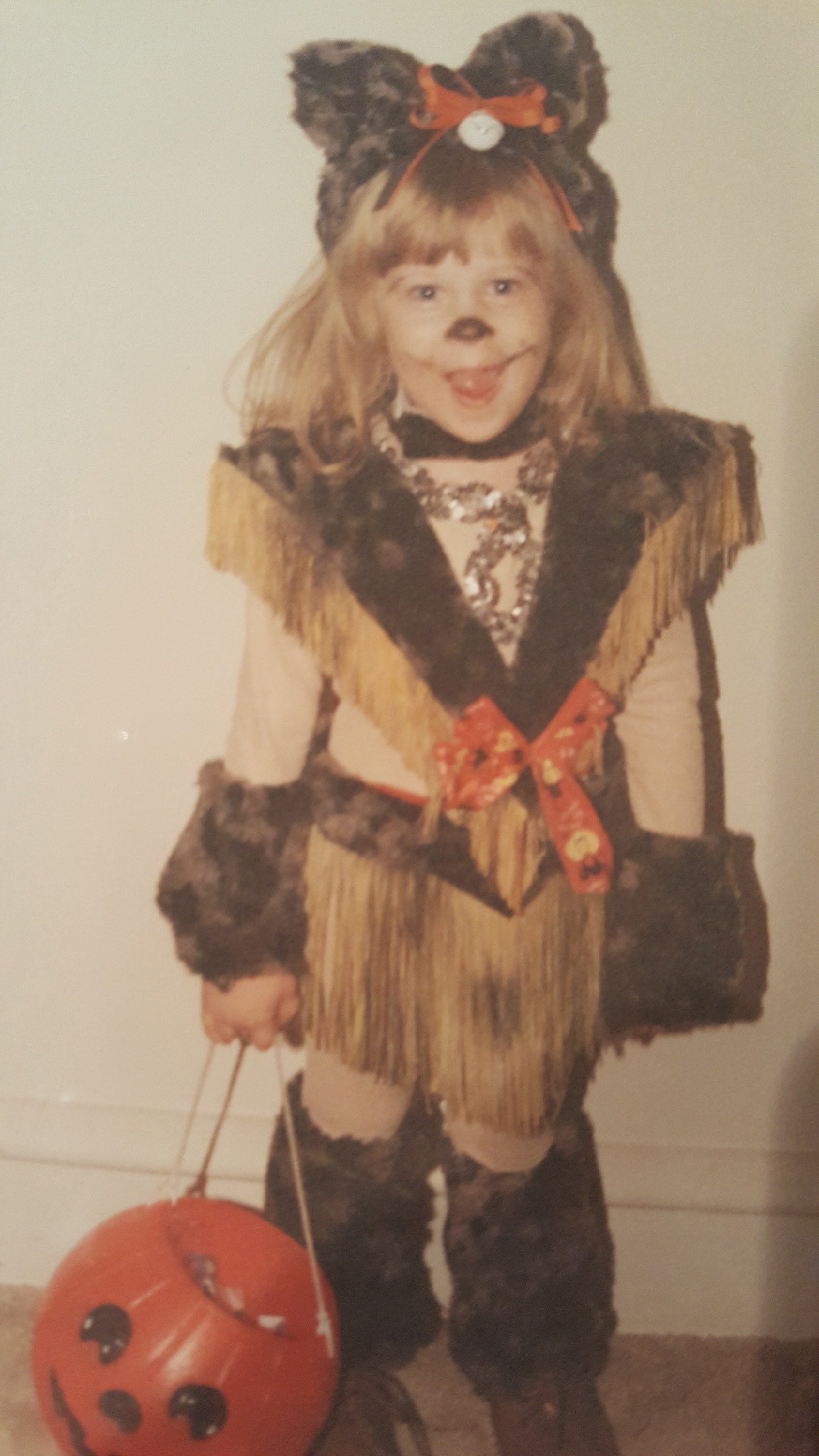 Young girl dressed as a cat, holding a plastic pumpkin full of candy.