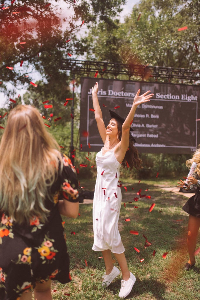 Woman wearing a Commencement cap raises her hands in celebration in a backyard graduation event