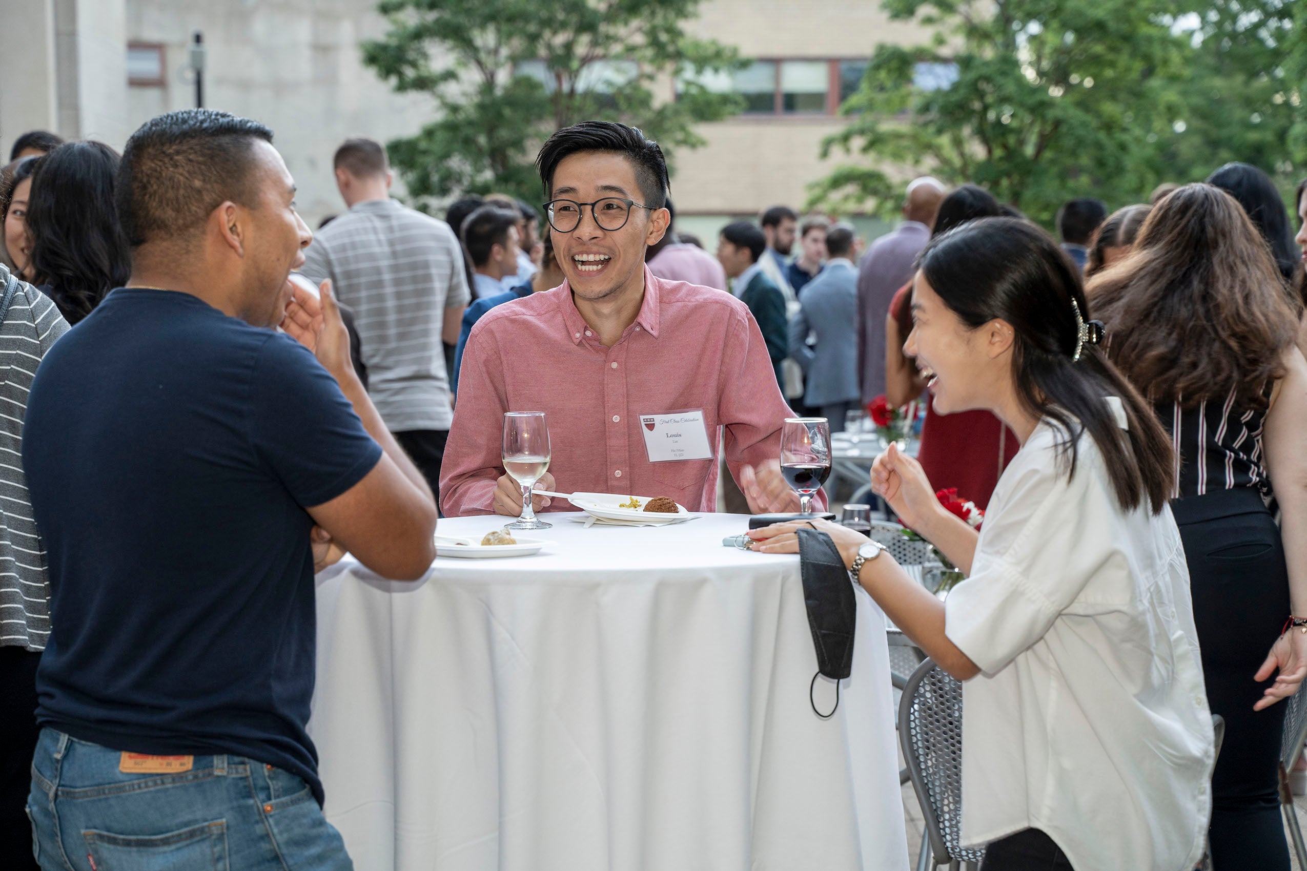 Three students standing outside at a table, eating and laughing.