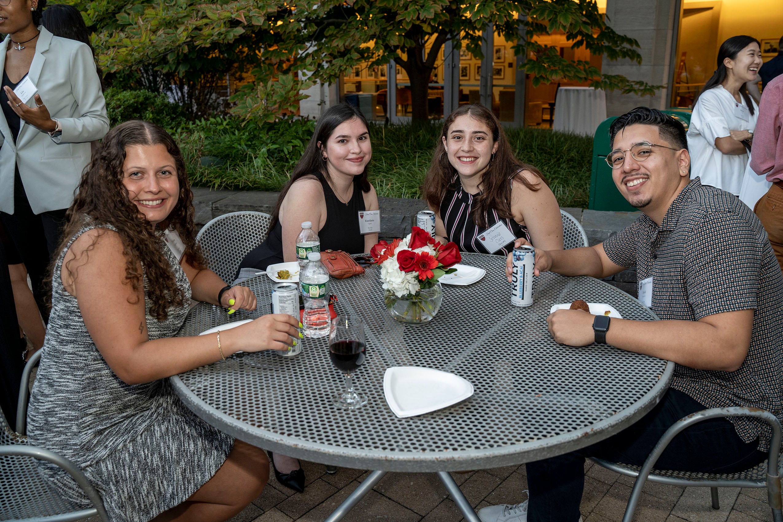 Four students sitting outside at a table, smiling for the camera.