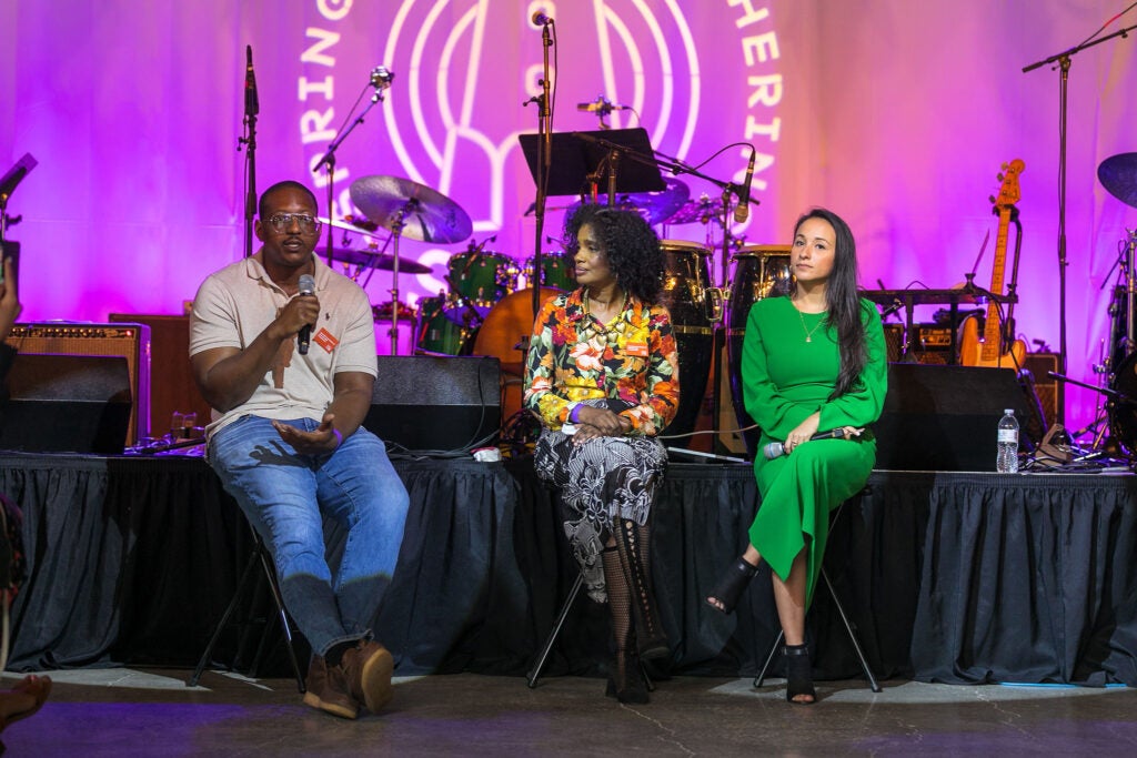 Three panelists, including Tylek, sit in front of a stage