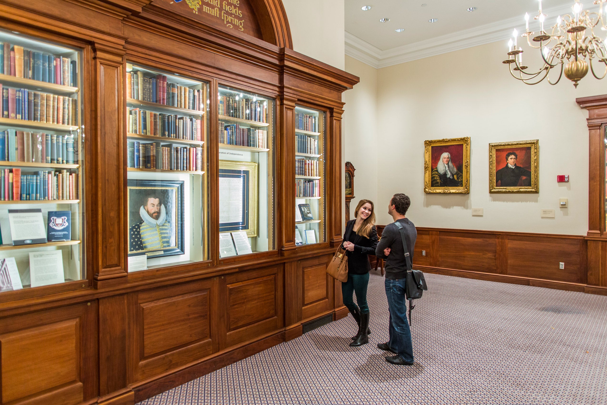 Two people standing in the Caspersen Room in front of the north wall bookshelf display