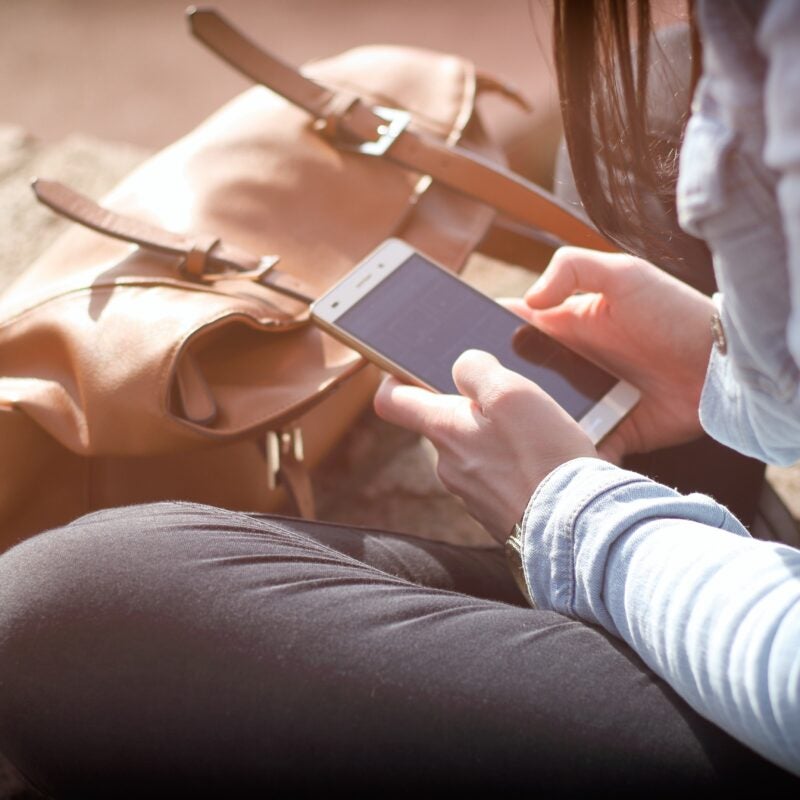 a person sitting down outside holding their cell phone