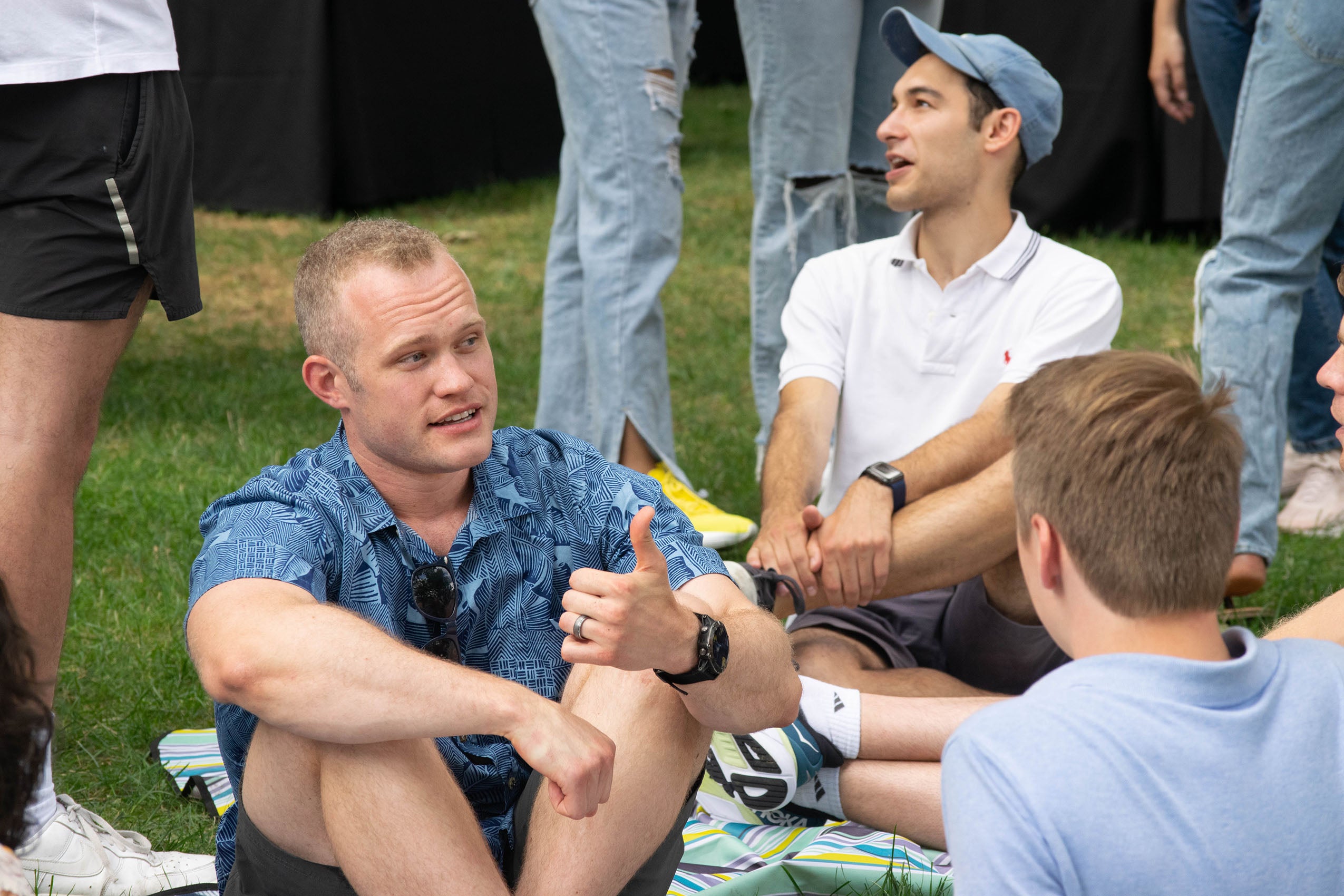 Three men sitting outside on the ground talking.