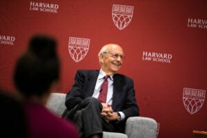 Stephen Breyer seated in a light colored chair in front of a crimson backdrop.