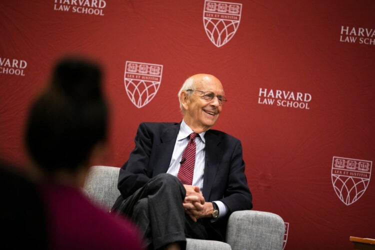 Stephen Breyer seated in a light colored chair in front of a crimson backdrop.