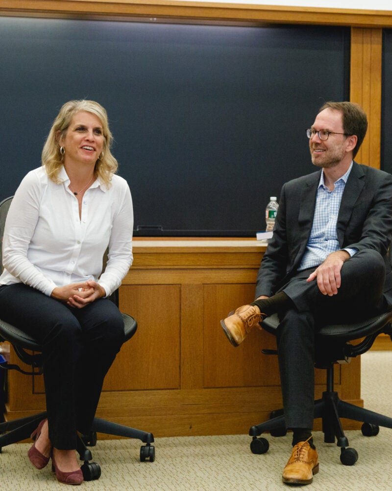 Two law professors, seated, in conversation in the front of a class room.