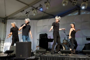 Several people in black t-shirts dance on a stage