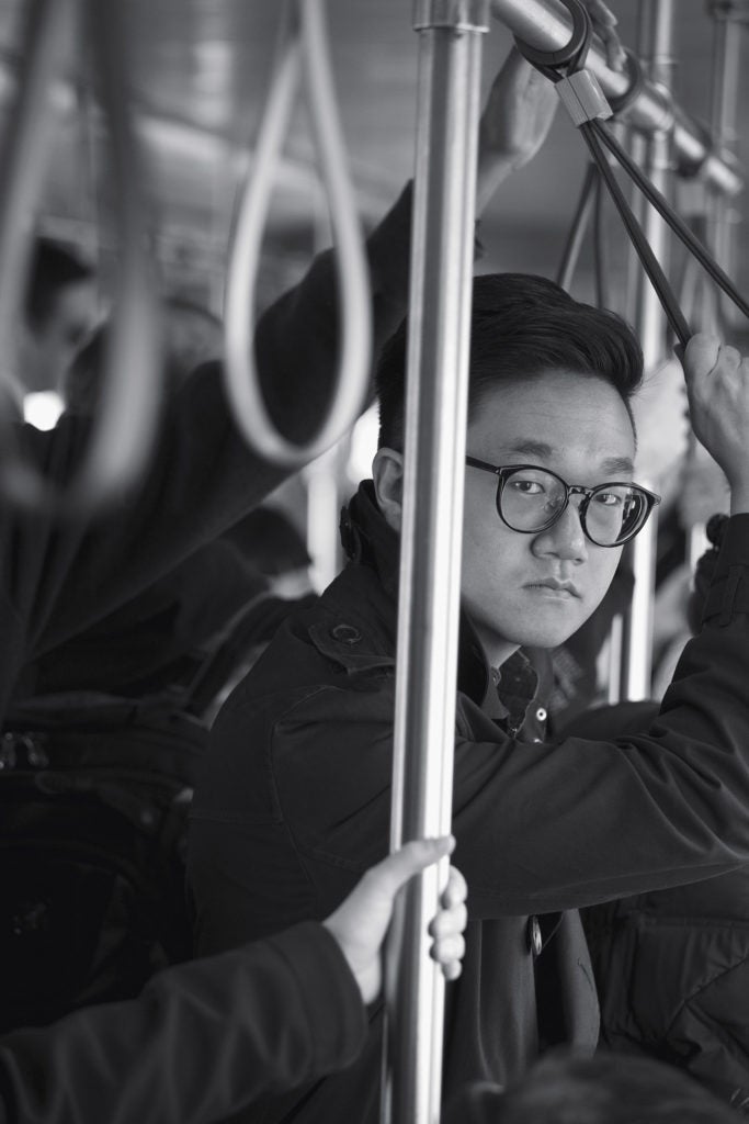 Man standing in a train holding onto overhead support