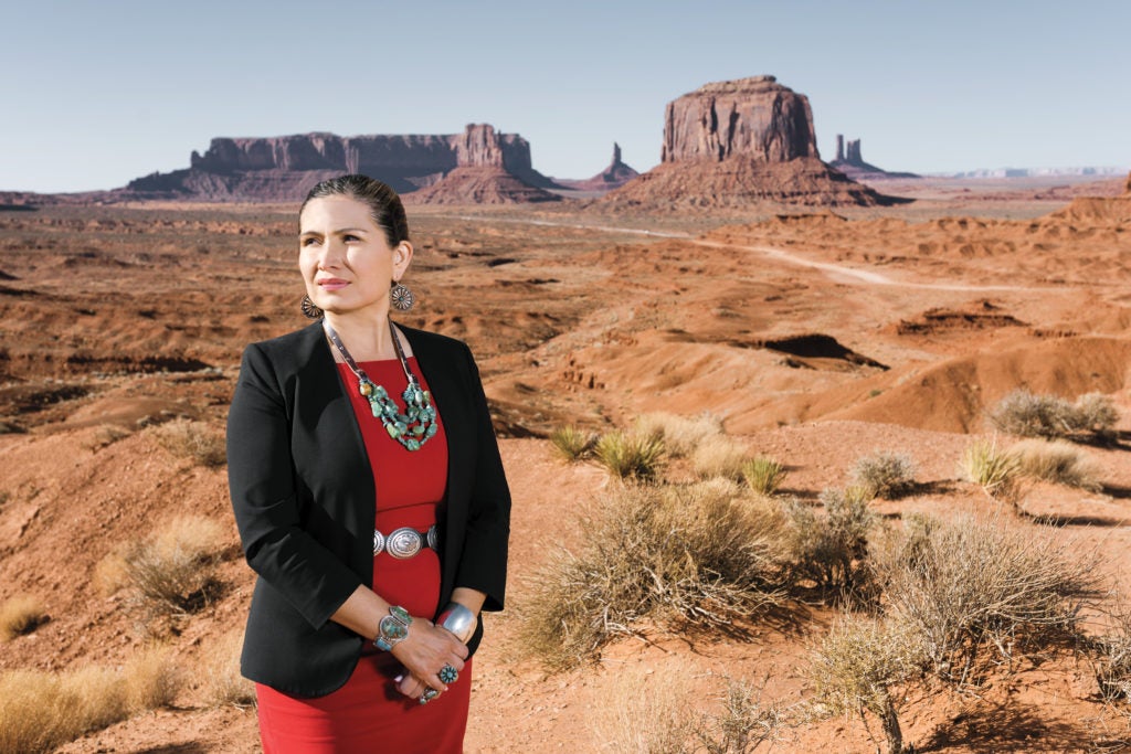 Woman wearing a red dress and black blazer standing with a desert in the background