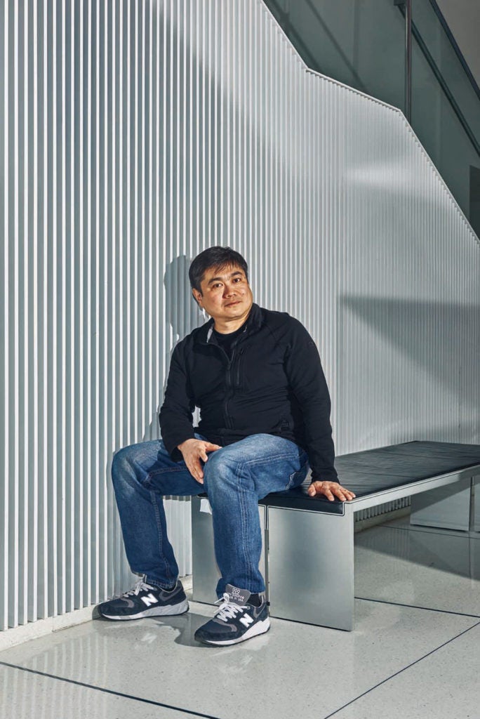Portrait of Joi Ito sitting on a modern steal bench