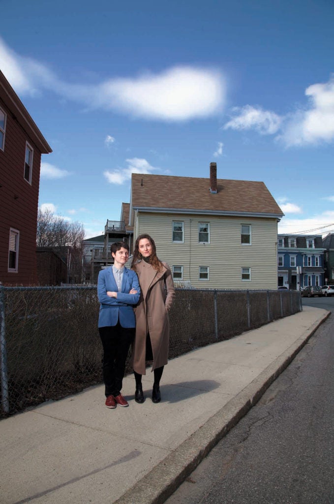 Two women standing on a sidewalk in a residential neighborhood