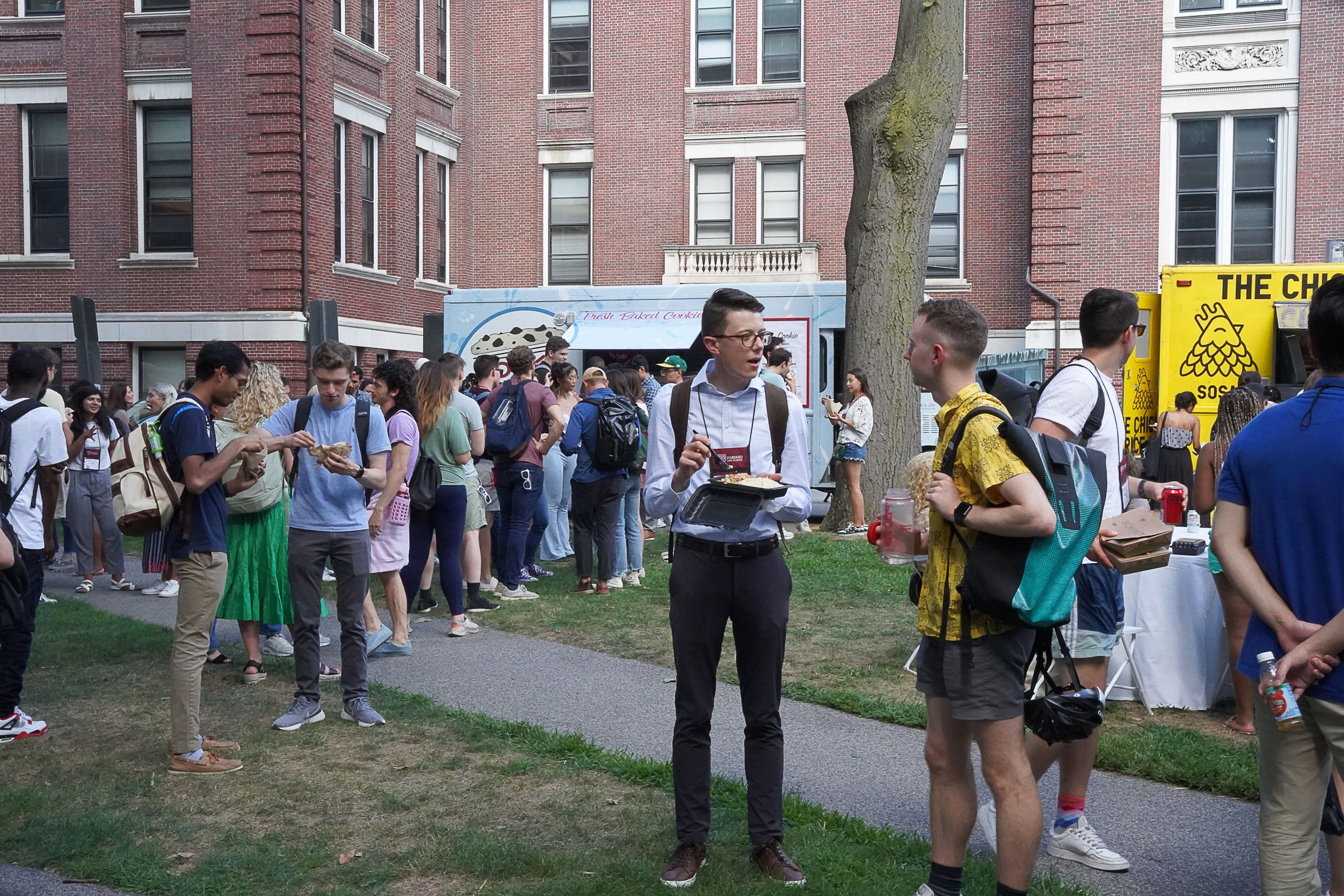 Students standing outside, talking and eating by two food trucks.