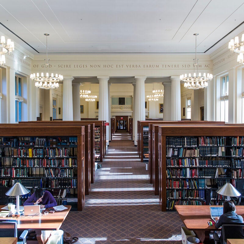 students working at tables in library with rows of books