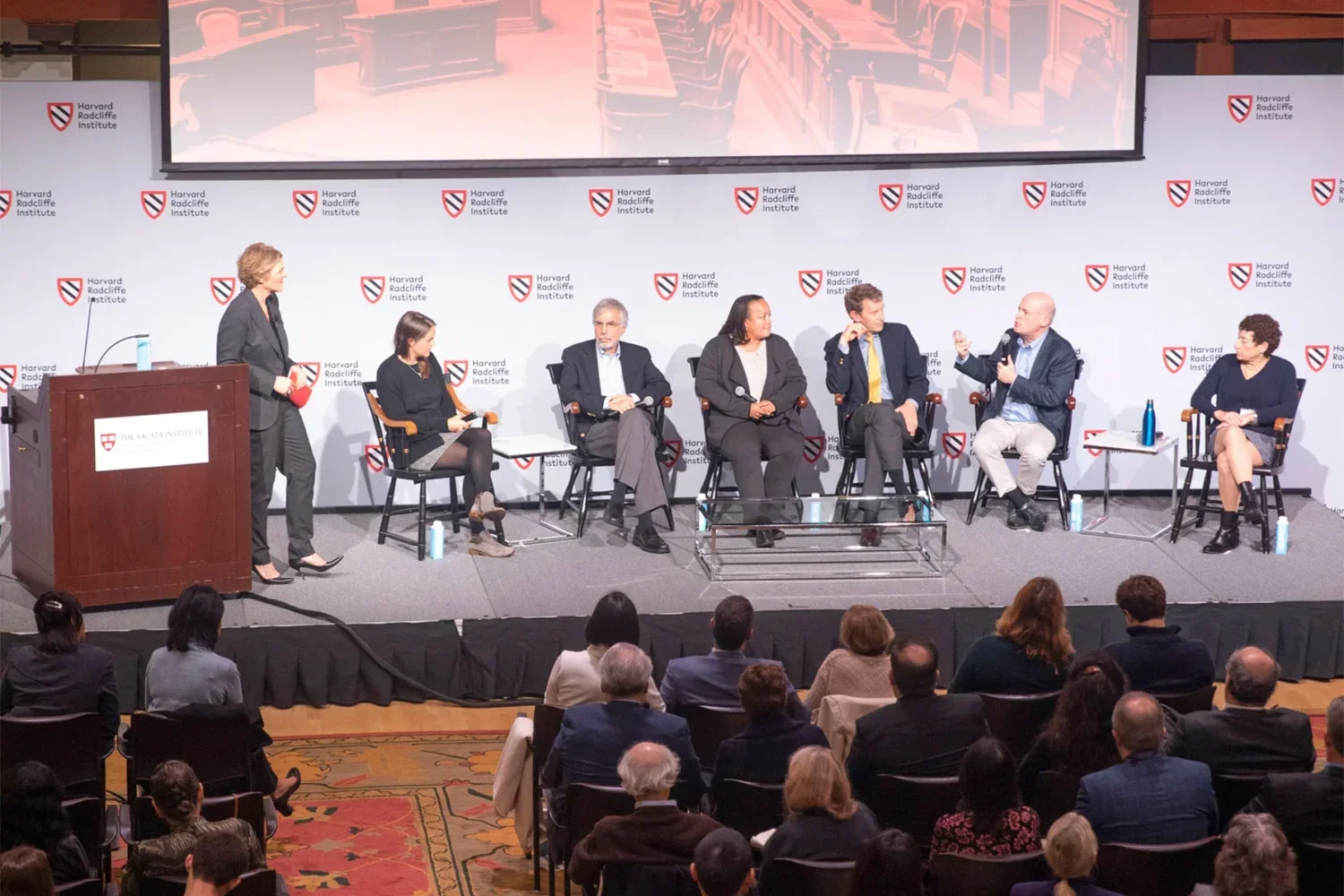panel of seven people on a stage in front of a crowd