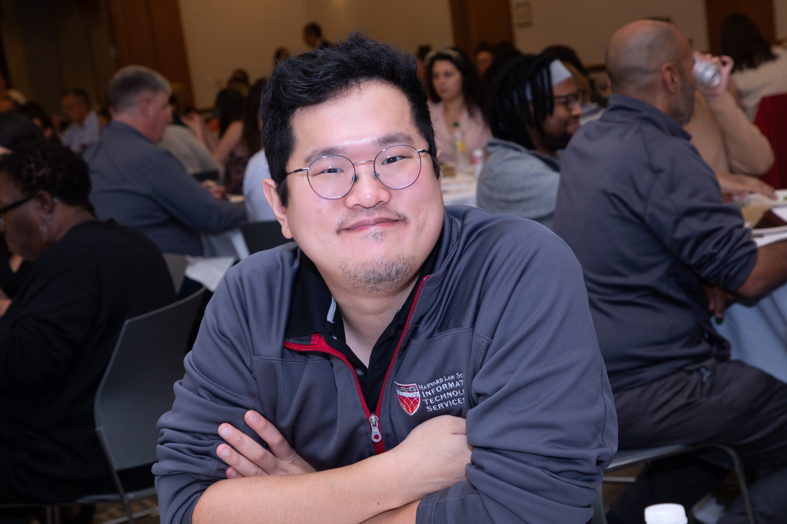 A close up of a man sitting at a table with his arms crossed looking at the camera