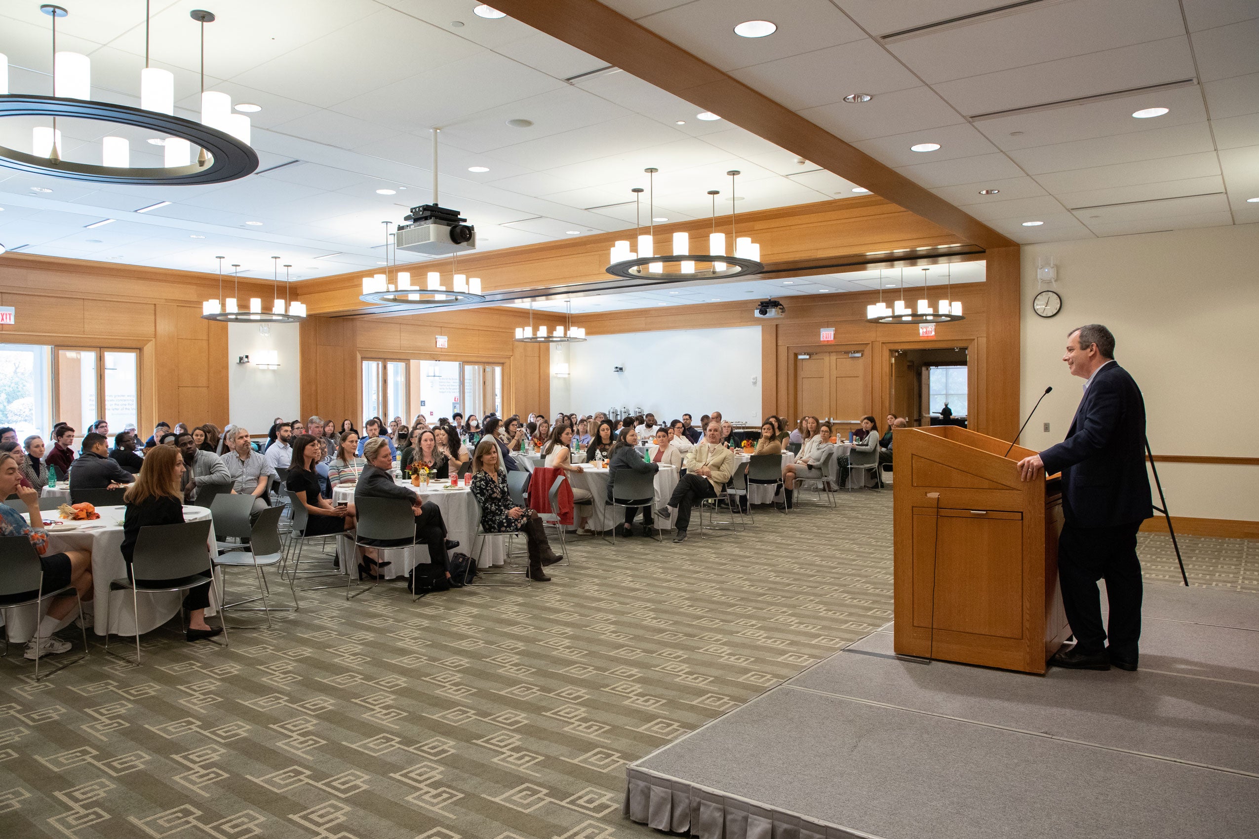 Dean Manning at a podium speaking to a room of people seated at round tables
