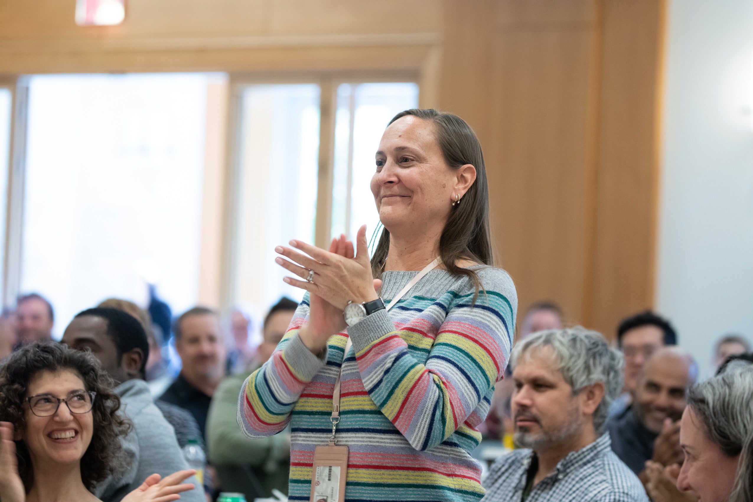 A woman standing up and clapping in a crowd