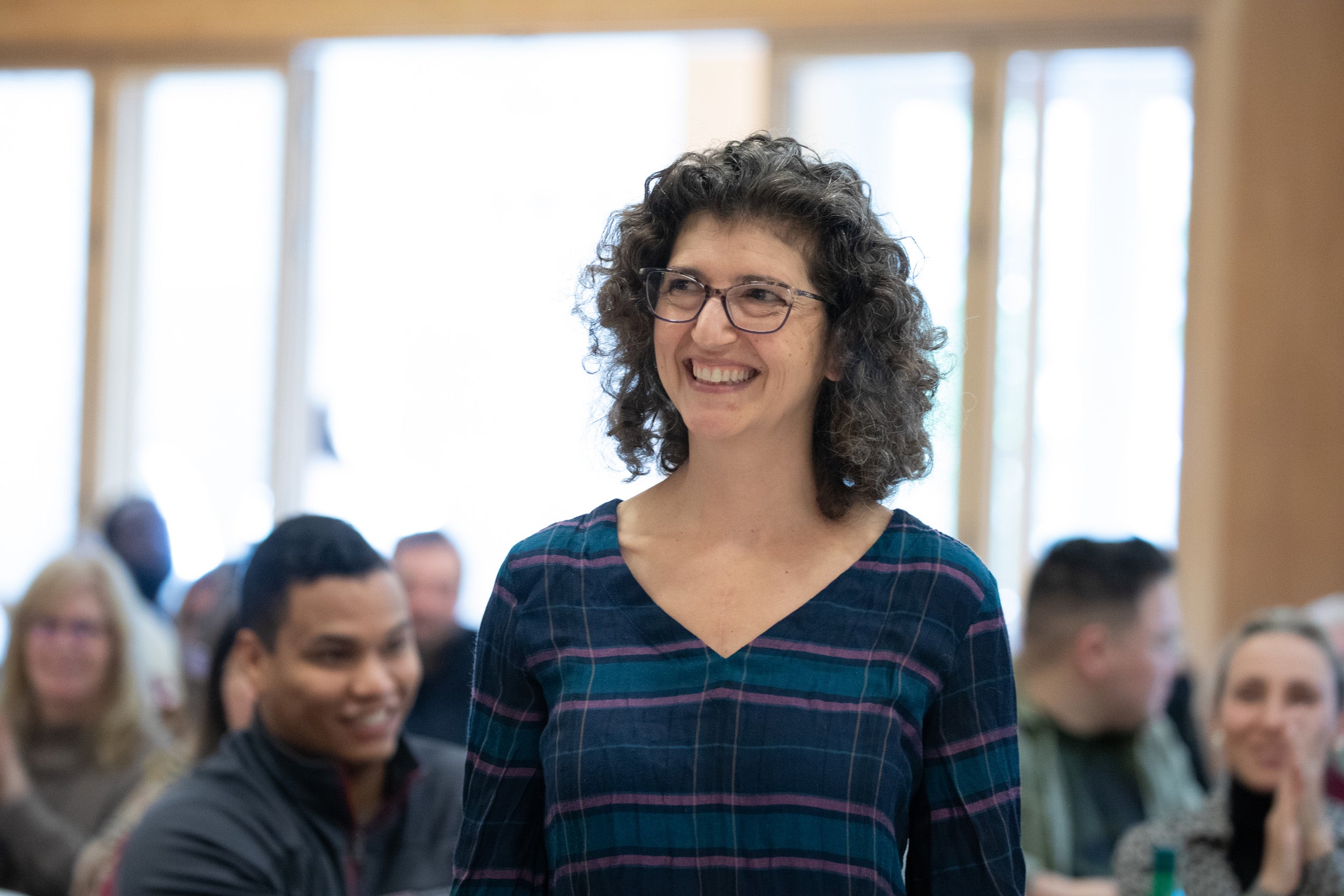 A woman with a smile standing up in a crowd in a room