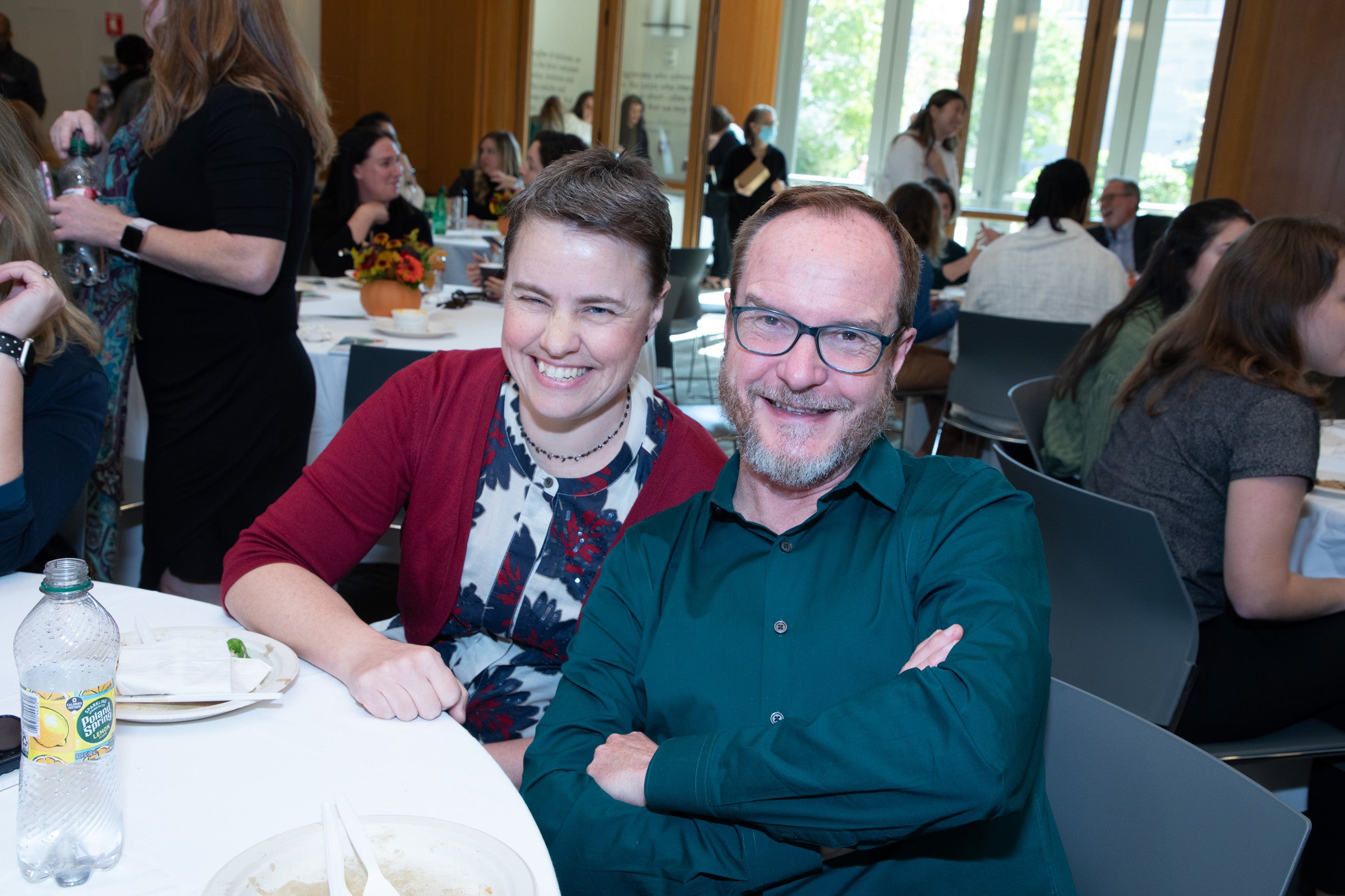Two people sitting at a table at an event smile for the camera