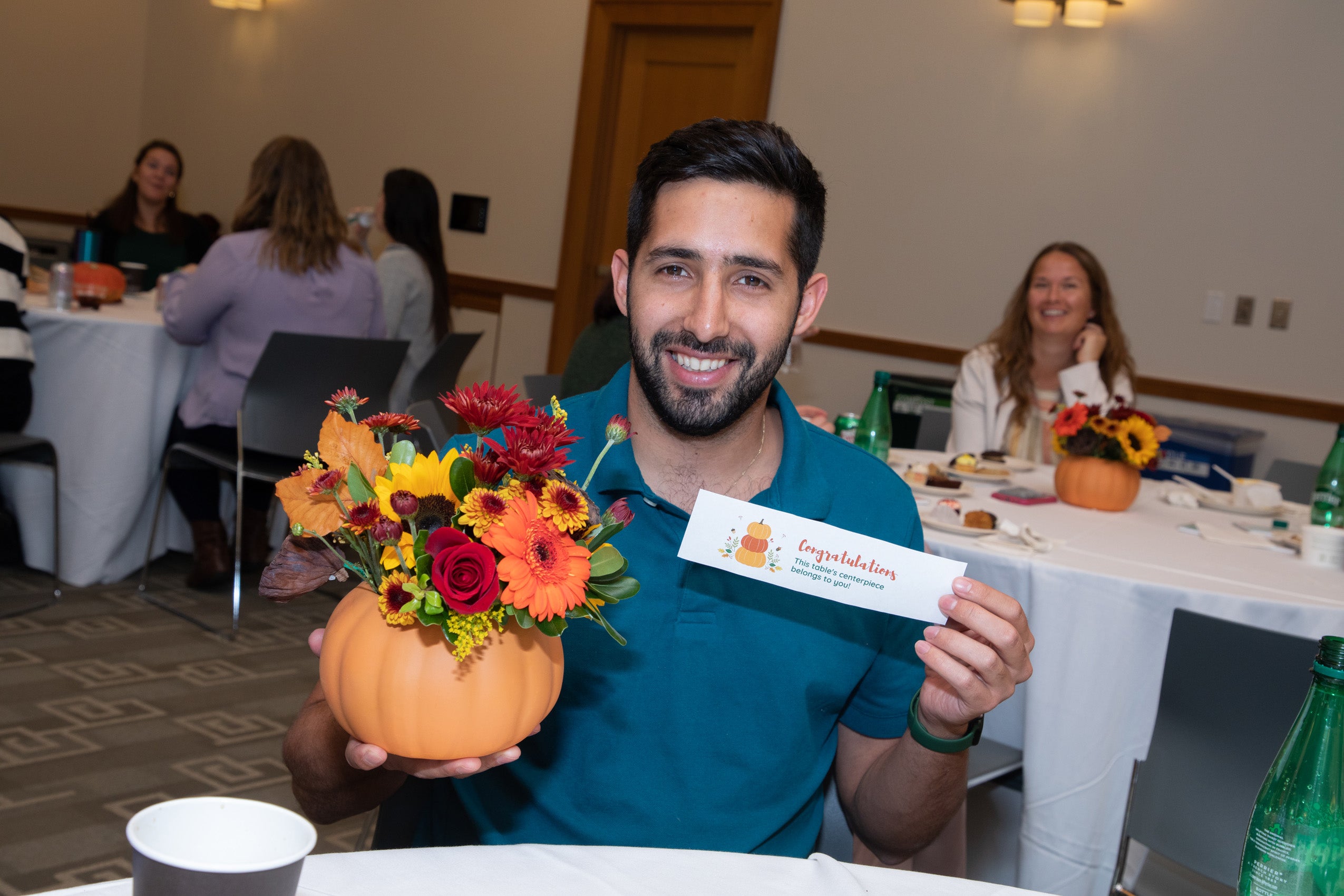 A man holding a congratulations note holds a fall flower arrangement