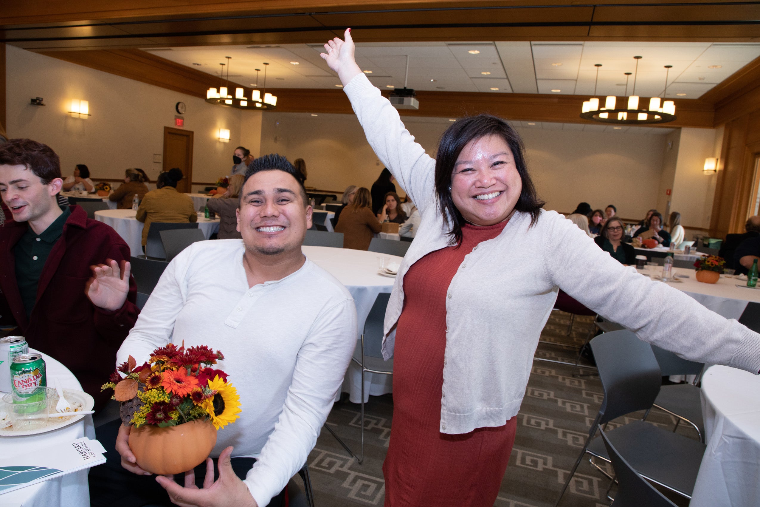 A man holds a fall flower arrangement and a woman standing nearby gestures happily