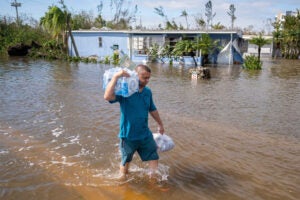 A man carrying bottled water wades through water in a flooded neighborhood.