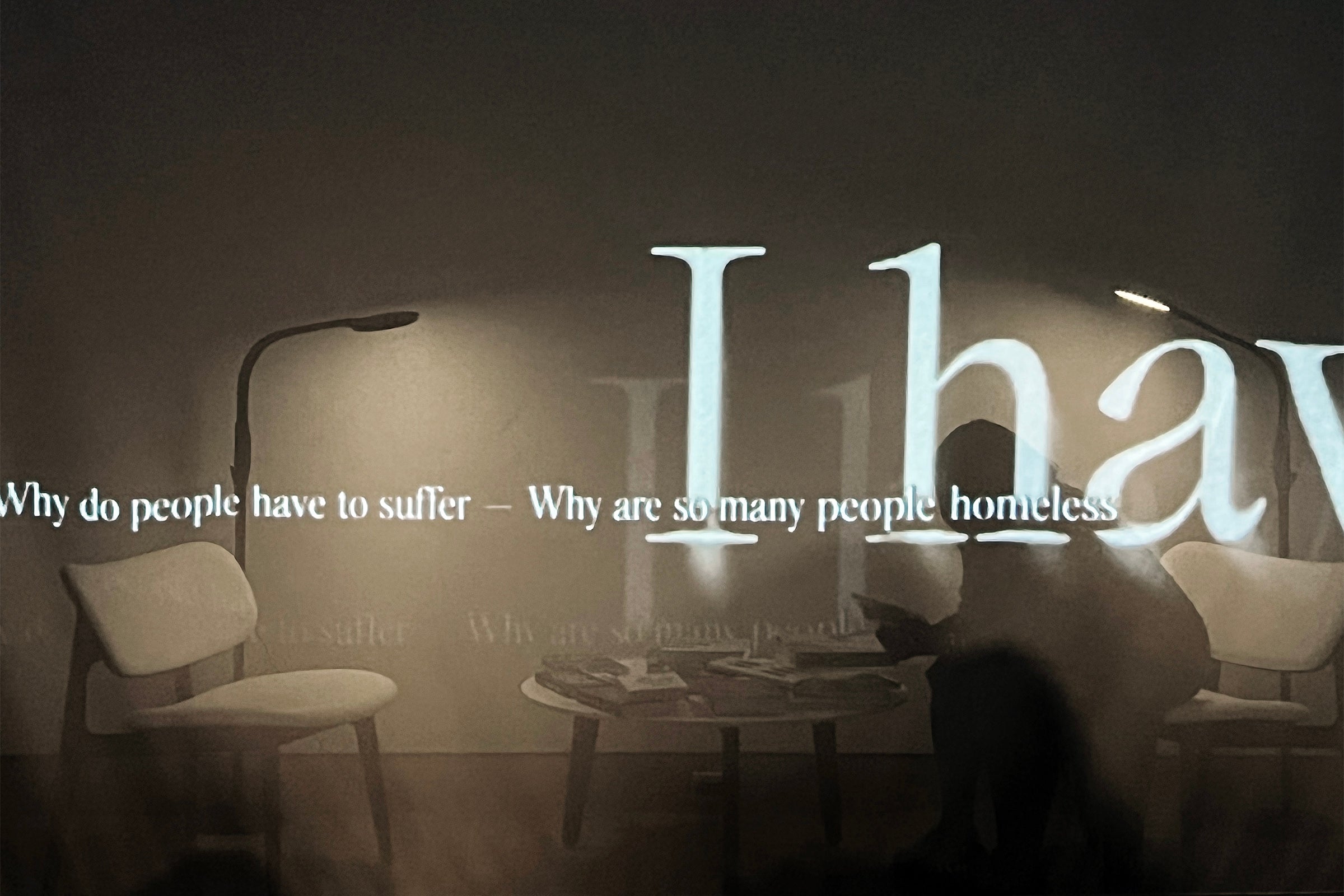 A person in silhouette sitting at a table behind a translucent screen with words projected onto it.