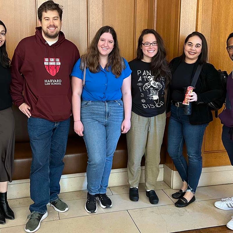Six students standing in front of a wood paneled wall, smiling for the camera.