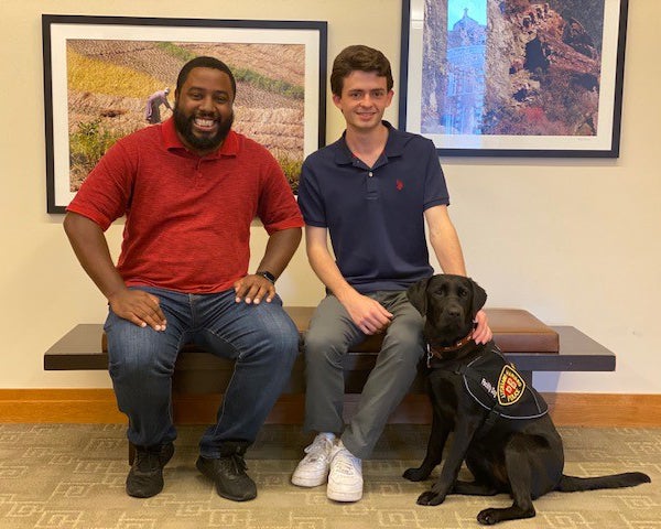 Two Harvard Law School staff members sit on a bench with Sasha, Harvard's community engagement dog.