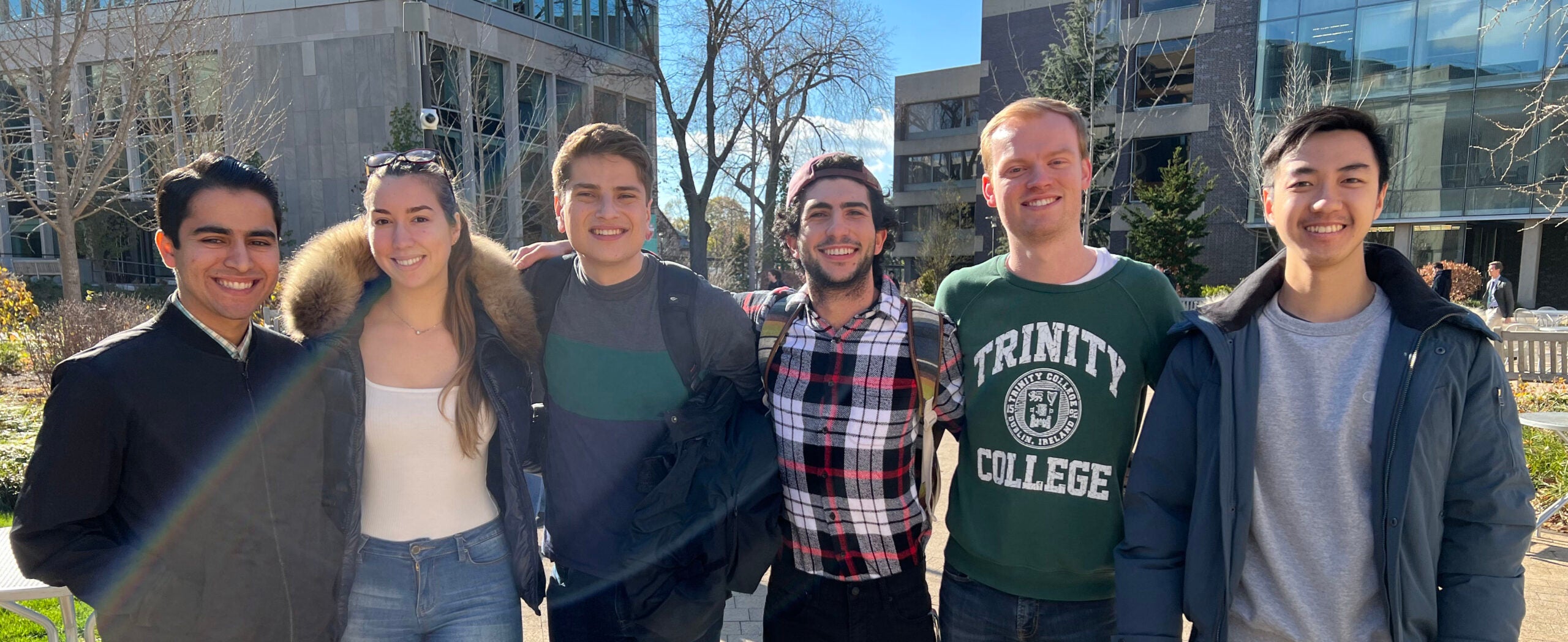 A group of six students stand close together outside, smiling for the camera.