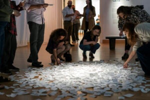 Several people gathered around and interacting with pieces of paper on the floor that are part of a museum exhibit..