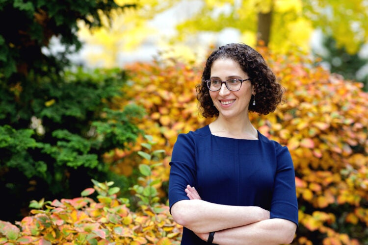 A woman in a blue dress poses in front of fall leaves on the Harvard Law School campus.