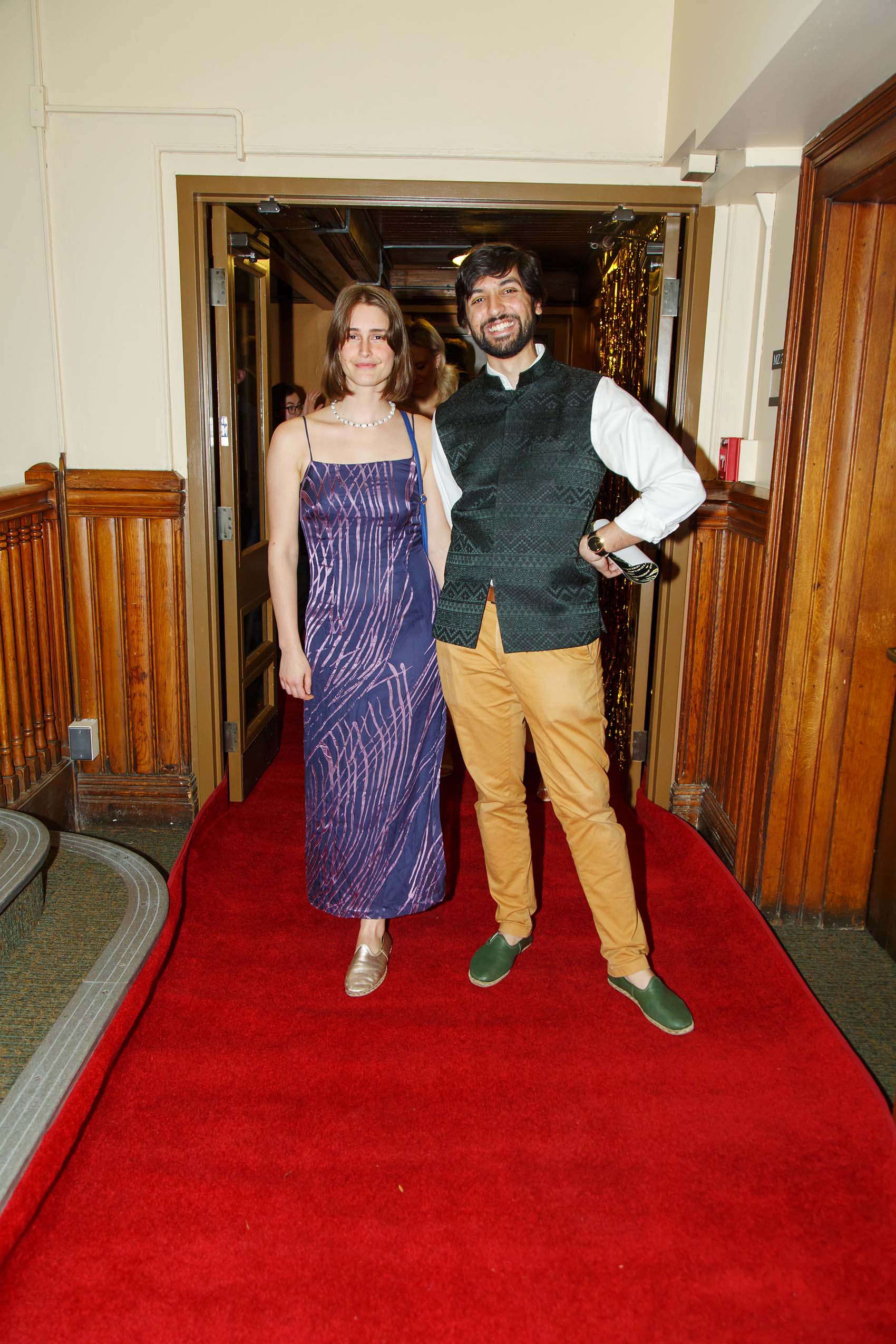 A man and woman dressed in formal attire pose on a red carpet.