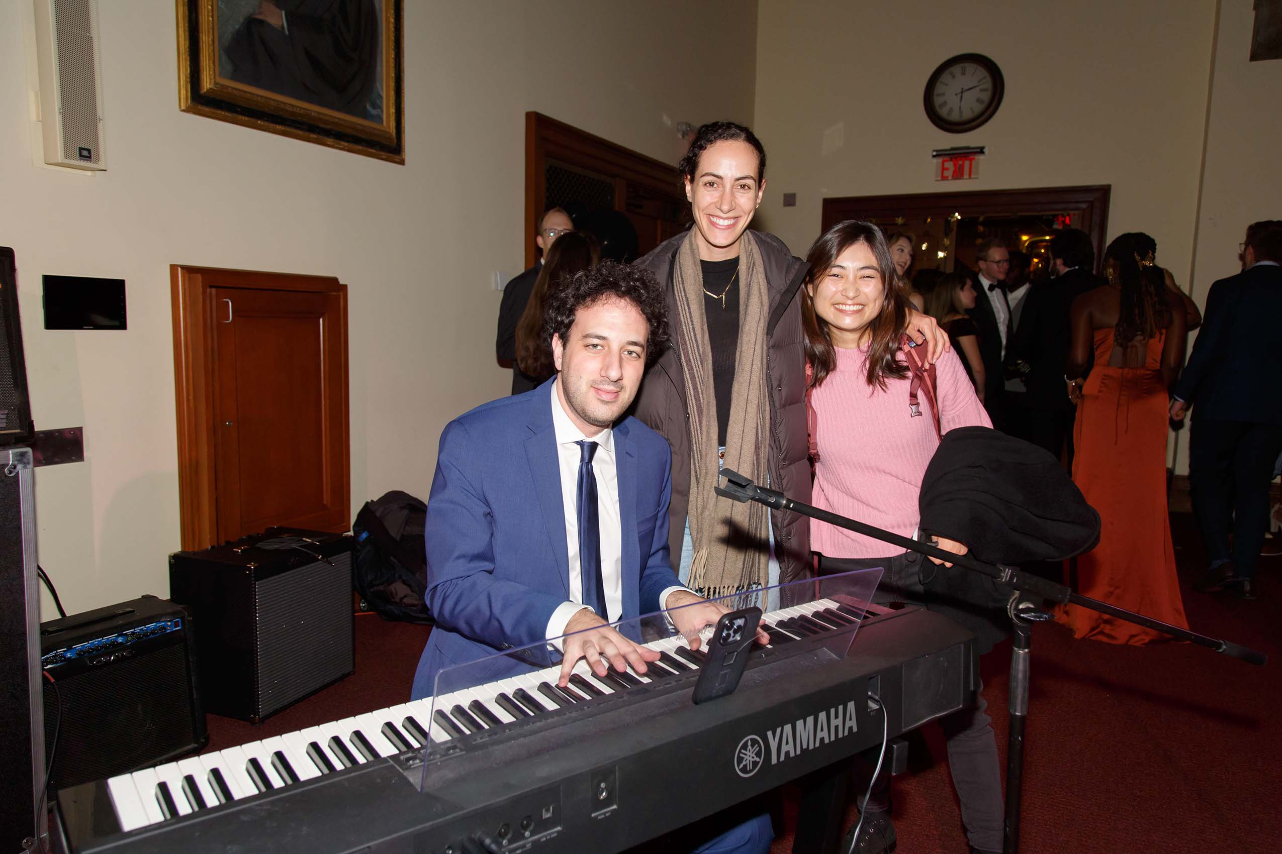 A man sit at keyboard. Two women standing next to him.