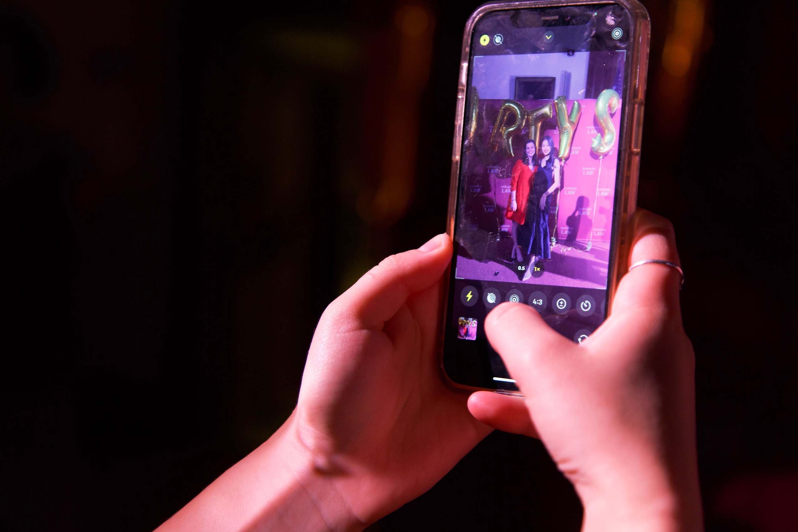 Close up up hands holding a mobile phone and taking a photo of to women in formal dresses.