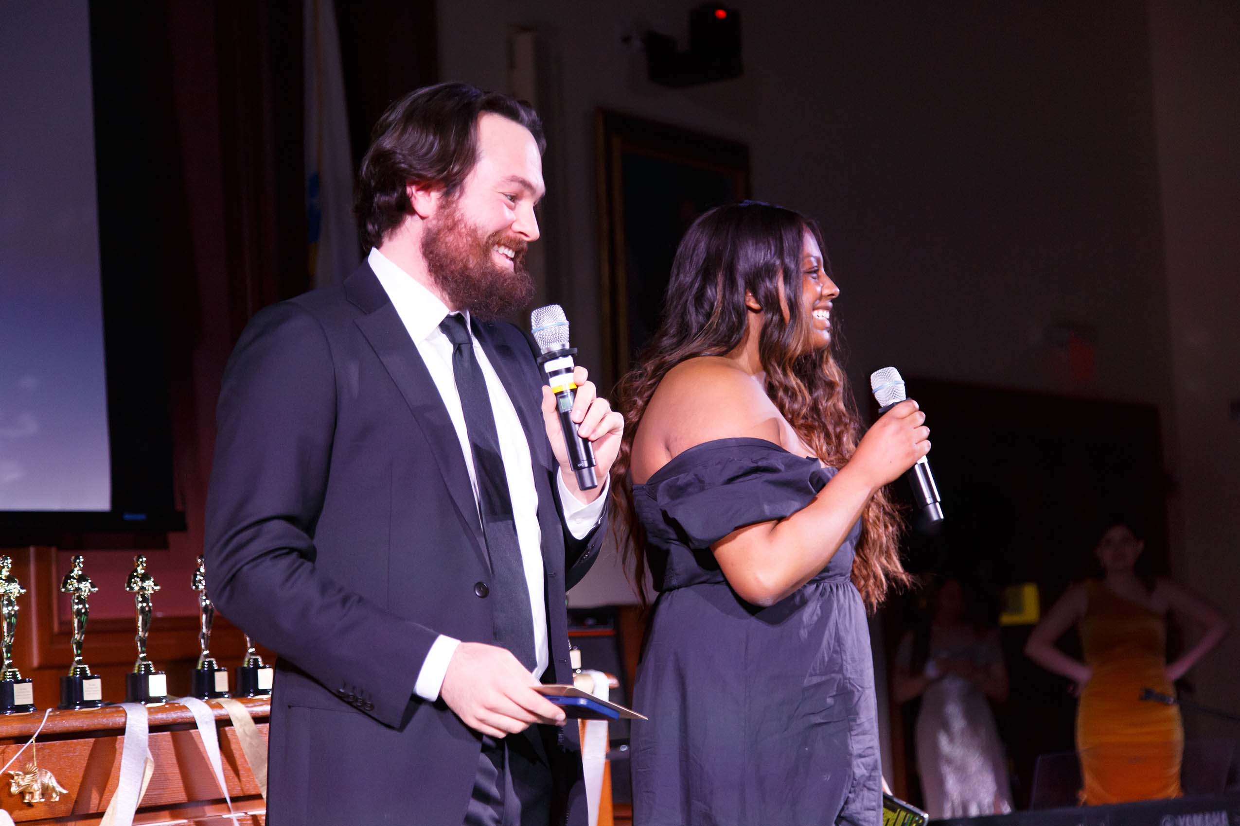 Two people in formal attire standing on stage holding microphones.