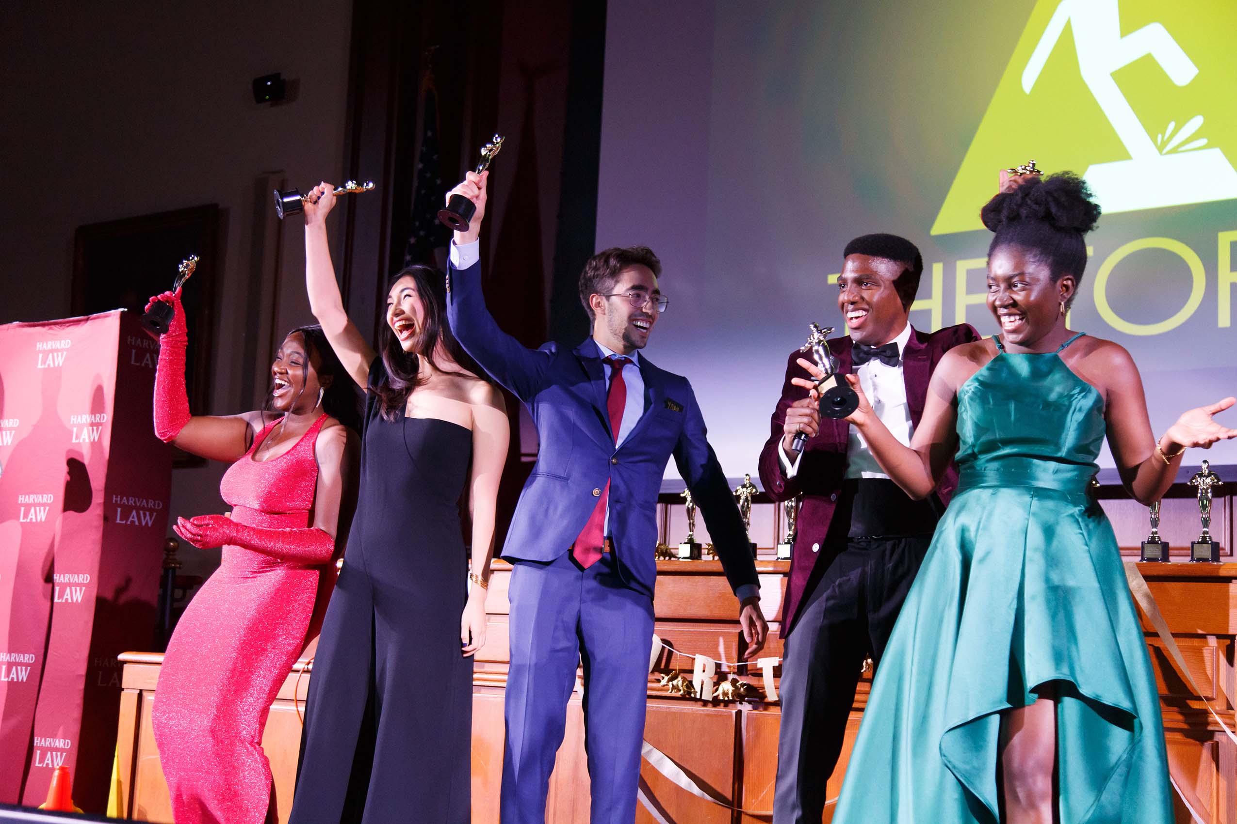 Three women and two men wearing formal attire standing on a stage holding awards and smiling.
