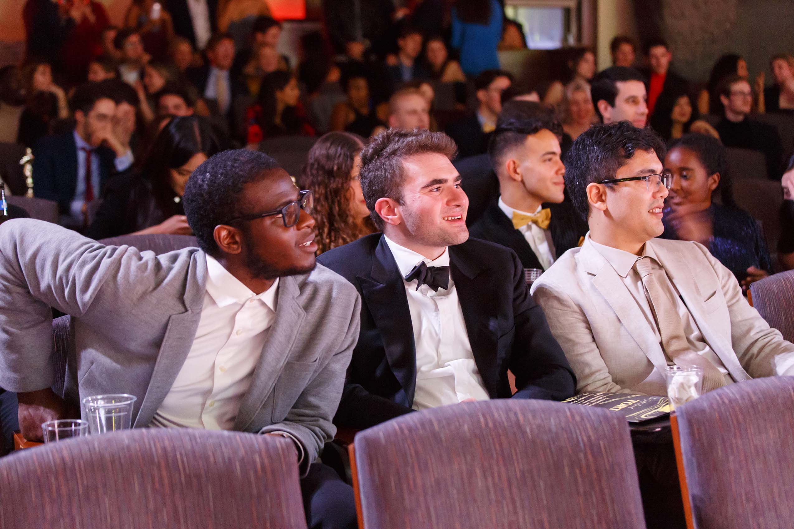 Focus on three students, wearing formal suits, in an audience.