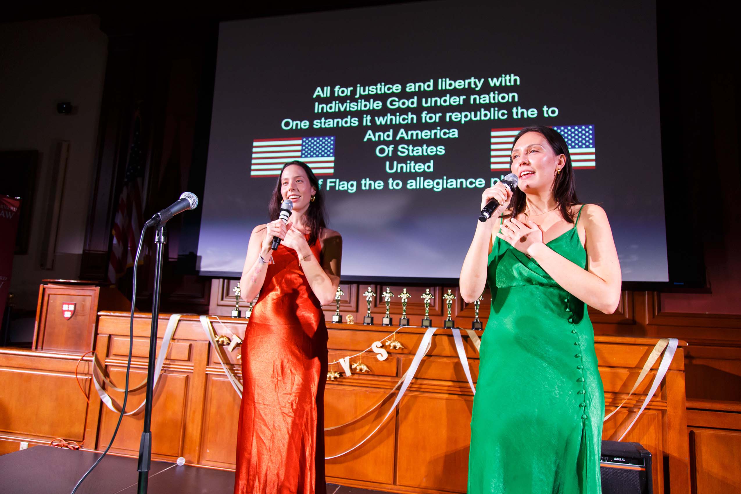 Two students wearing formal dresses with microphones on stage.