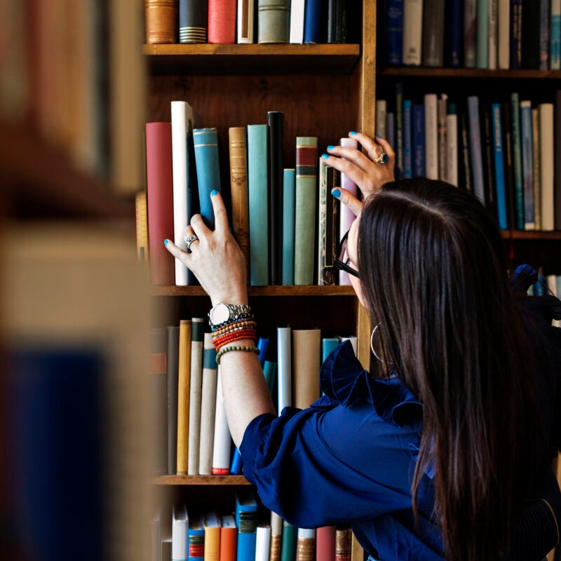 A person searching for a book on a bookshelf..