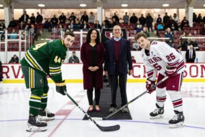 William Alford and Lakshmi Clark stand at center ice with two hockey players, preparing for the puck drop.