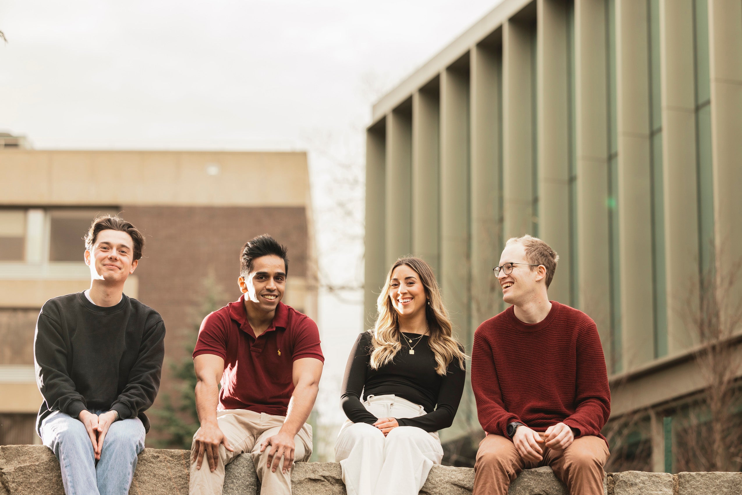 Four students sitting on a stone wall on campus