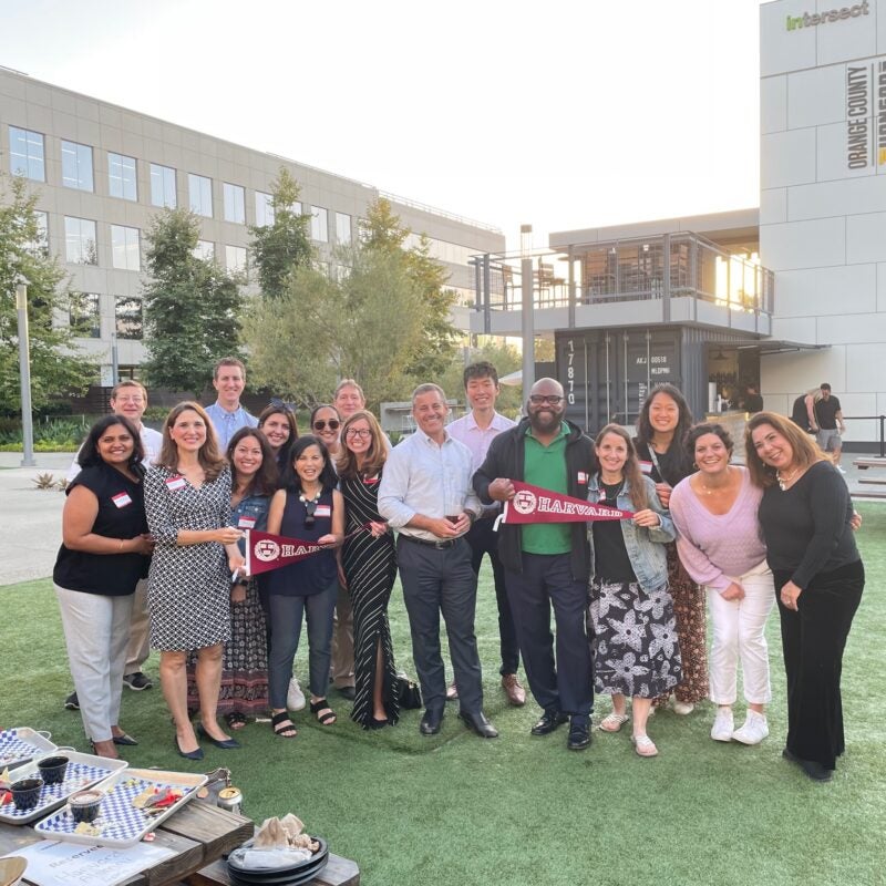 A group of people posing together holding Harvard pennants.
