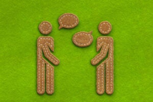 Two figures speaking on a green felt background.