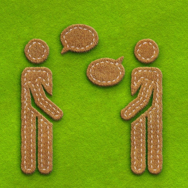 Two figures speaking on a green felt background.